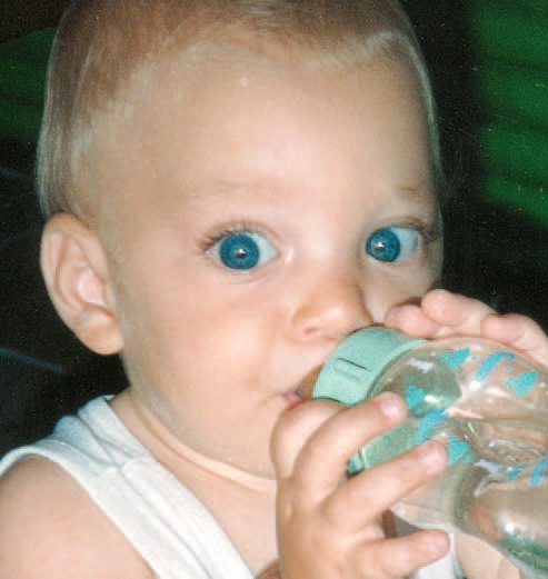A toddler with big blue eyes drinking from a bottle
